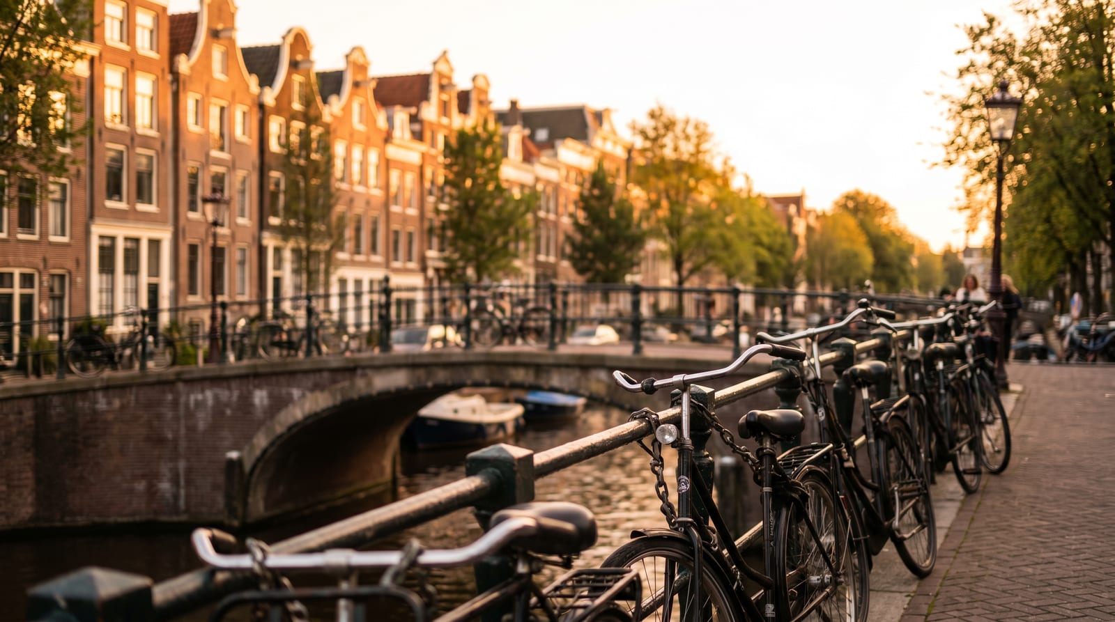 Canal din Amsterdam cu case înguste, biciclete pe pod și bărci, într-o lumină caldă de după-amiază