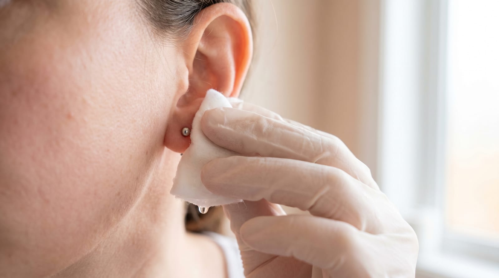 Curățarea blândă a unui piercing la ureche cu ser fiziologic și un disc de bumbac curat
